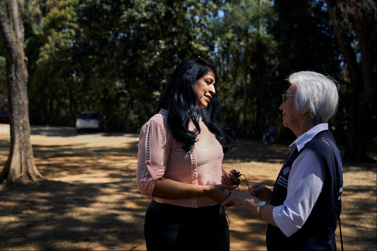 Dos mujeres se toman de la mano mientras conversan en un jardín a la sombra
