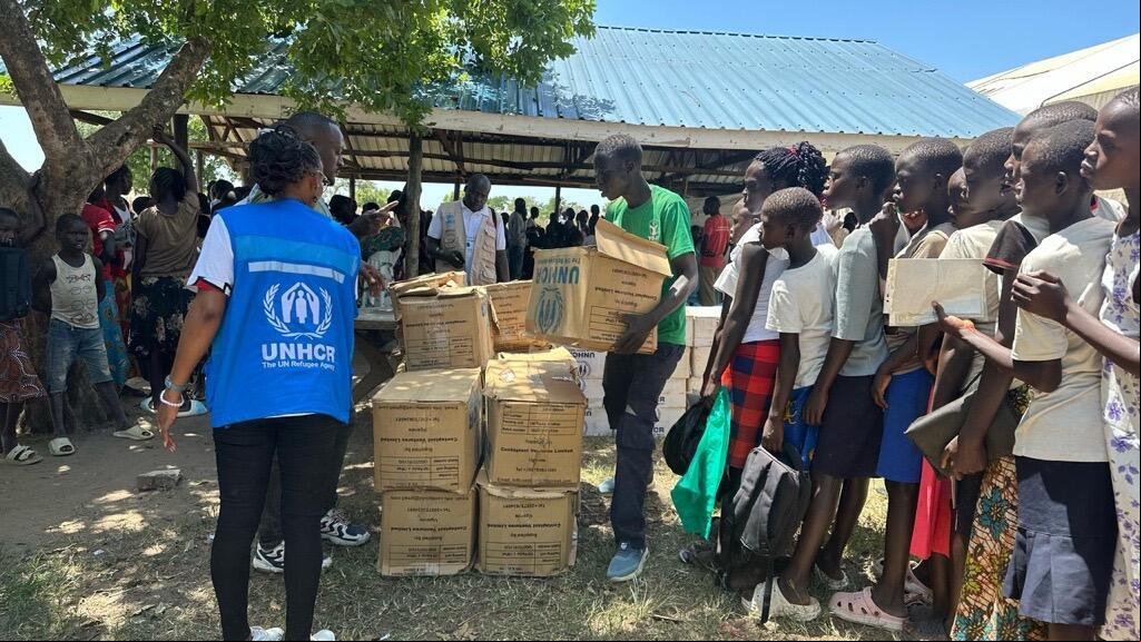 Mujeres, niñas y niños hacen fila para recibir paquetes de ayuda en cajas de cartón por parte de un miembro del personal de ACNUR