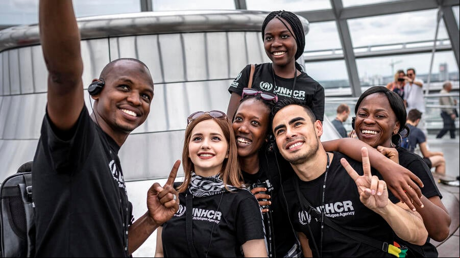 Un grupo de personas jóvenes, que llevan playeras de ACNUR, se toman una selfi. Un grupo de personas jóvenes, que llevan playeras de ACNUR, se toman una selfi.