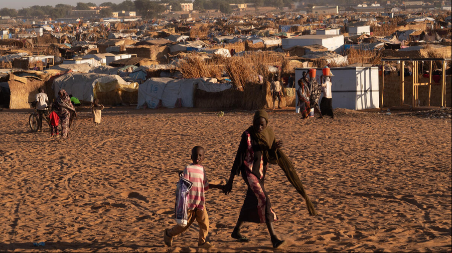 Tomados de la mano, una mujer y un niño caminan frente a un asentamiento de refugiados
